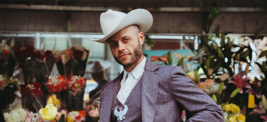 Charley Crockett wearing a cowboy hat standing in front of flowers.