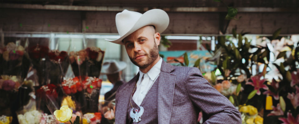 Charley Crockett wearing a cowboy hat standing in front of flowers.
