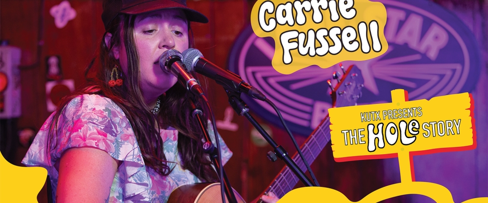 Carrie Fussell sings into a microphone and plays guitar
